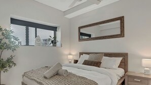 A bedroom with a wooden bed, a nightstand, a mirror, and a window with a plant.