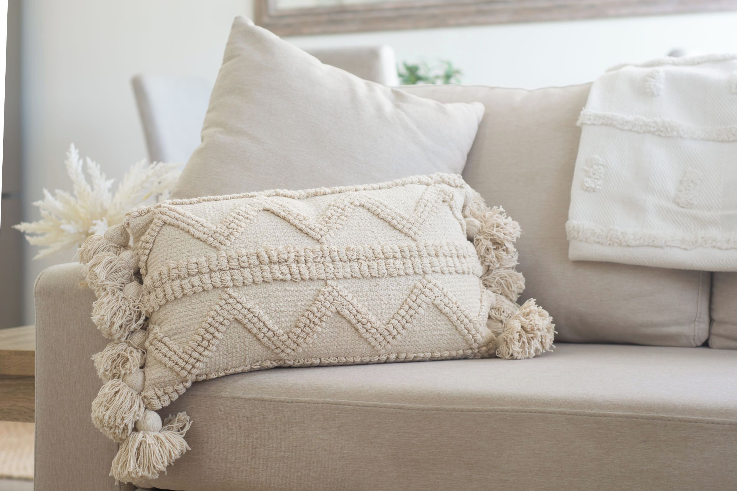A beige sofa with a textured throw blanket and a decorative pillow.