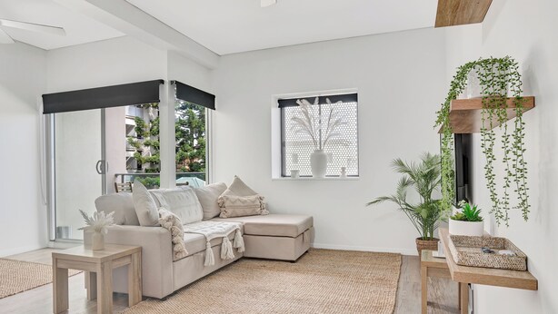 A modern living room with a sectional sofa, a small table, a woven rug, and a wall-mounted shelf with plants.