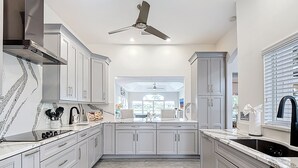 A modern kitchen with white cabinets, a black countertop, and a ceiling fan. - Wally's Fairway To Haven: Discover Your Paradise: Rental with Lake View, Pool, and Golf Access! (Cape Coral)