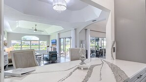 A spacious living area with a large white marble countertop, a chandelier, and a view of a pool and outdoor seating area. - Wally's Fairway To Haven: Discover Your Paradise: Rental with Lake View, Pool, and Golf Access! (Cape Coral)