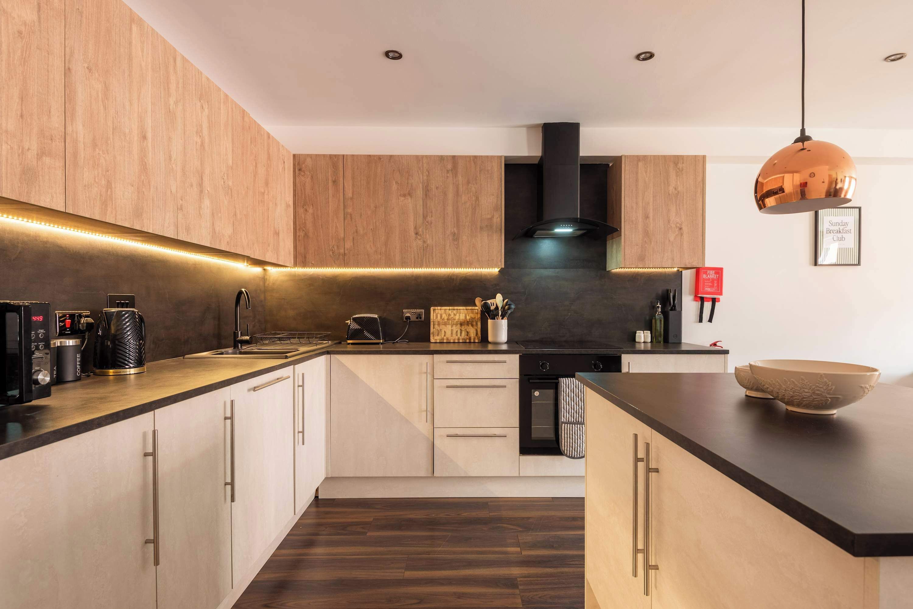 A modern kitchen with wooden cabinets, a black stove, and a copper pendant light.