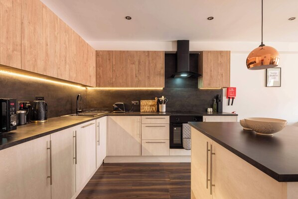 Une cuisine moderne avec des meubles en bois, une cuisinière noire et un luminaire suspendu en cuivre.