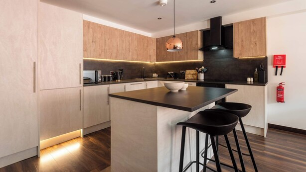 A modern kitchen with a central island, wooden cabinets, and black bar stools.