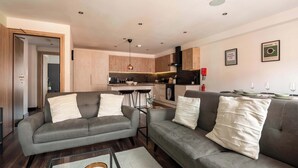 A modern living room with a grey sofa set, a glass coffee table, and a kitchen in the background.