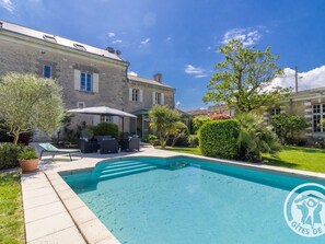 Ein Schwimmbad mit einer Terrassenanlage, Gartenmöbeln und einem großen Gebäude im Hintergrund.