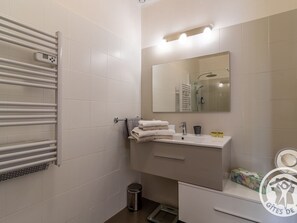 A modern bathroom with a white tiled wall, a built-in towel rack, a sink with a mirror, and a shower area. - Charming Stay with Pool in Loire Valley's Wine Region (Doué-en-Anjou)