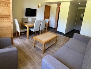 Una sala de estar moderna con una mesa de centro de madera, sofás grises y un área de comedor con televisor y sillas.