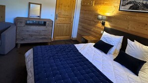 A bedroom with a wooden headboard, a bed with a quilted duvet and pillows, a wooden dresser, a mirror, and a door. - Renovated 2-Room Ski-In/Ski-Out Apt with Pool & Wellness Center (Belle Plagne)