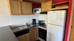 A compact kitchen with wooden cabinets, a microwave, a toaster, a coffee maker, and a dishwasher. - Renovated 2-Room Ski-In/Ski-Out Apt with Pool & Wellness Center (Belle Plagne)