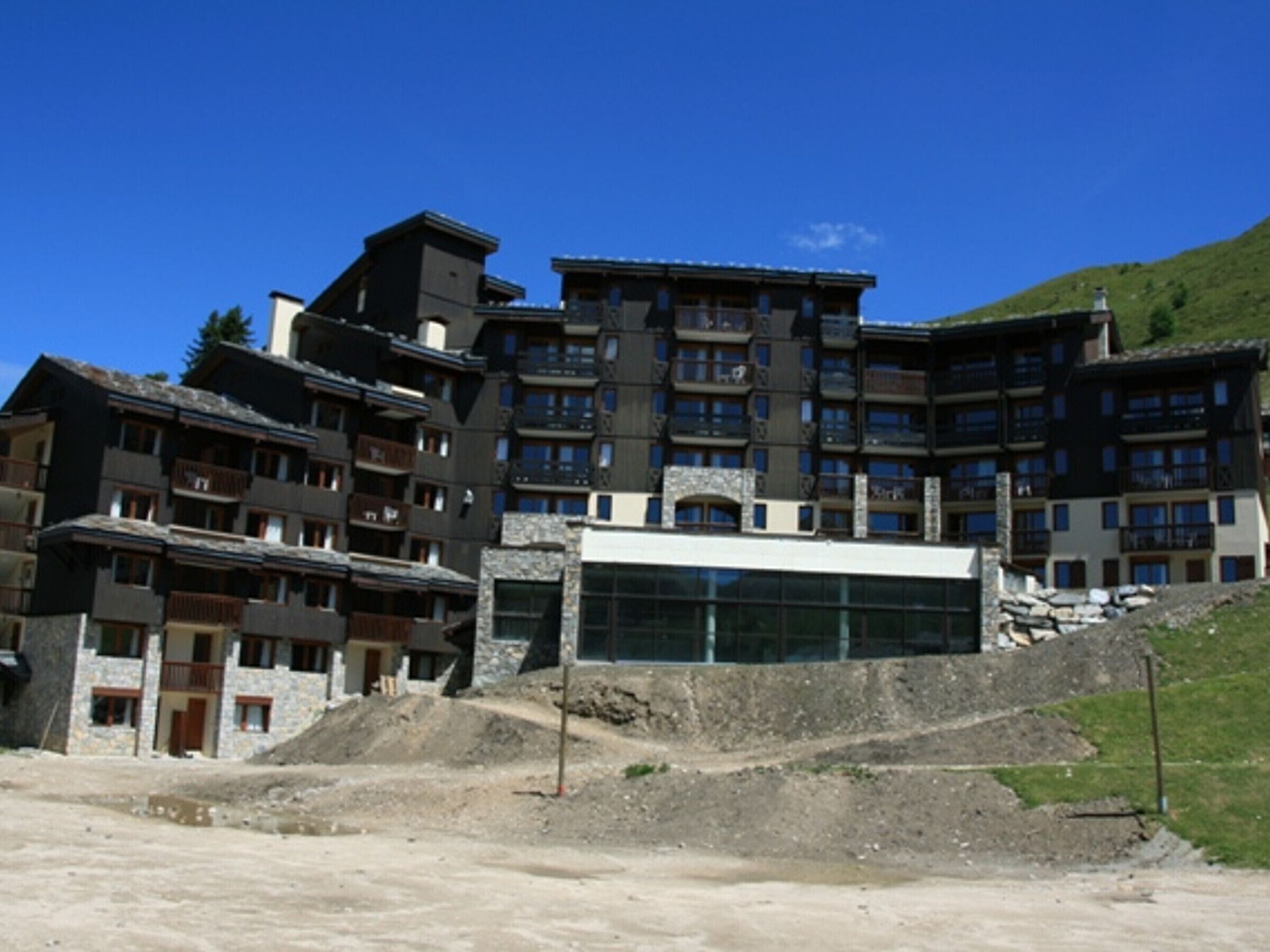 Un hôtel à plusieurs étages, doté de balcons, d’une façade centrale en verre et situé dans un cadre vallonné.