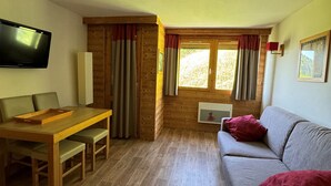 Ein gemütliches Zimmer mit einem Holzespeisetisch, einem grauen Sofa und einem an der Wand befestigten Fernseher.