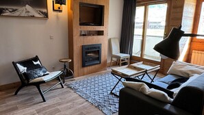 A modern living room with a fireplace, a sofa, a chair, and a TV mounted on the wall. - 3BR Apartment · 70m² · Ski-in/Ski-out · Pool · Pets allowed (Belle Plagne)