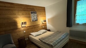 A bedroom with a wooden headboard, a bed with a plaid blanket, a chair, and a small rug. - 3BR Apartment · 70m² · Ski-in/Ski-out · Pool · Pets allowed (Belle Plagne)
