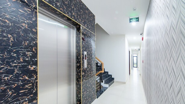 Un ascensor moderno con detalles de mármol, una escalera con barandillas de madera y un pasillo con paredes de diseño.