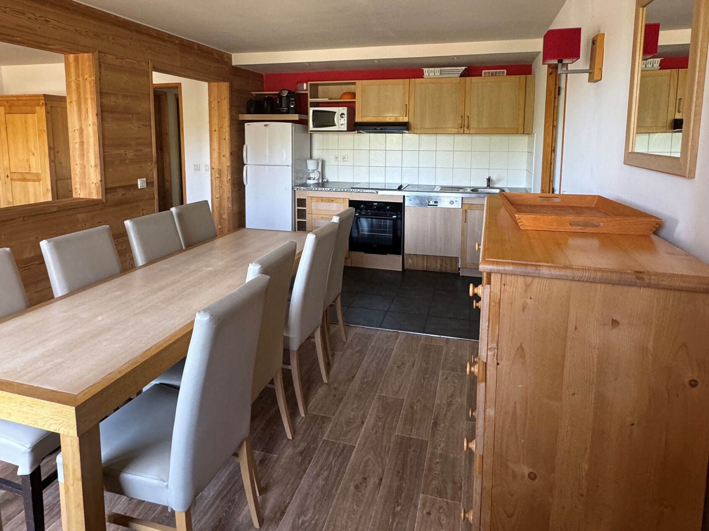 A compact kitchen with a dining area, wooden cabinets, a refrigerator, a microwave, and a dishwasher.
