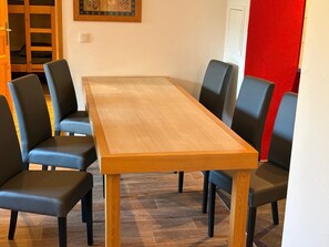 Een rechthoekige houten tafel met zes zwarte stoelen, een rode muur en een houten deur op de achtergrond.