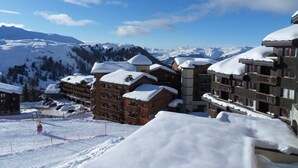 A snow-covered mountain resort with multiple buildings, including a large lodge with balconies and a ski slope in the foreground.
