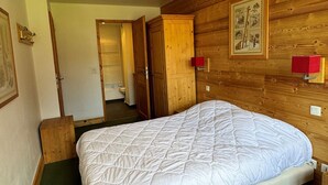A bedroom with a wooden headboard, a white quilted bedspread, a green carpet, and a wooden wardrobe with a red object on top.