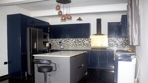 A modern kitchen with dark blue cabinets, a central island with a bar stool, a tiled backsplash, and a built-in oven. - Exclusive Villa - 5str Hideout, Private Pool, Wifi (Accra)