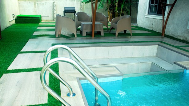 A swimming pool with a metal ladder, surrounded by a patio area with chairs and a small table. - Exclusive Villa - 5str Hideout, Private Pool, Wifi (Accra)