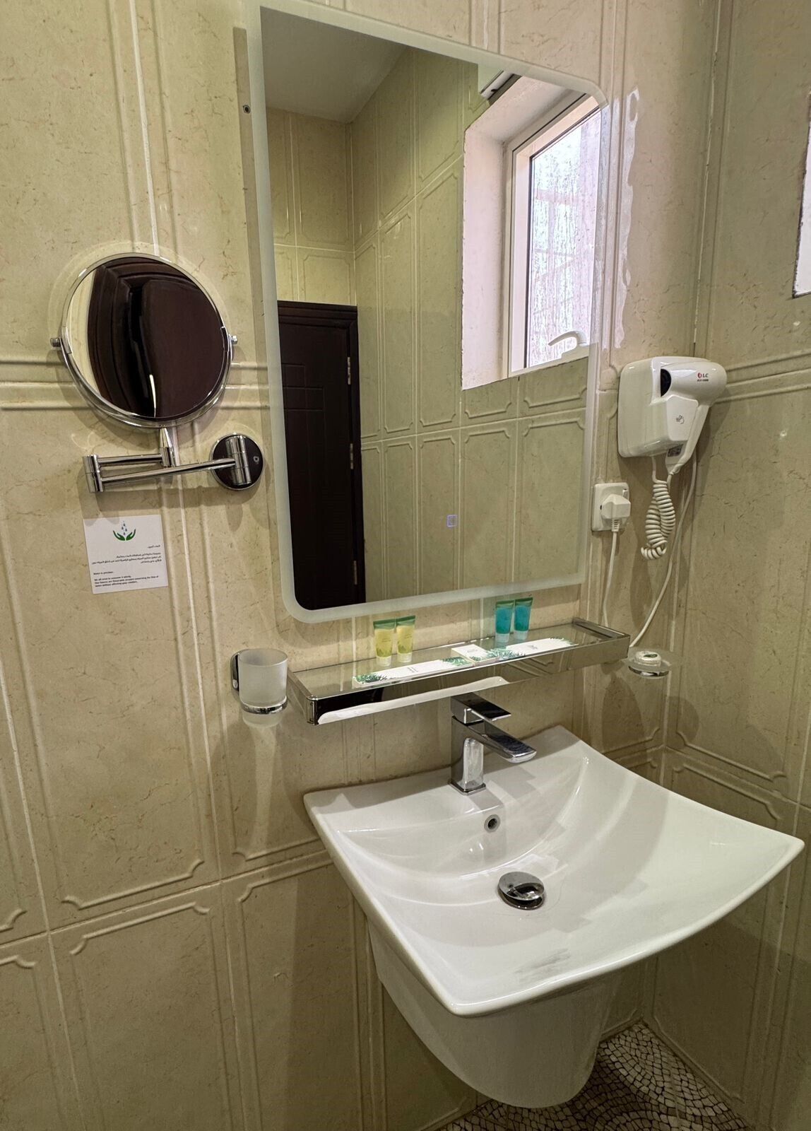 Ein Badezimmer mit einem weißen Waschbecken, einem runden Spiegel, einem Föhn und einem Ablagefach für Toilettenartikel.