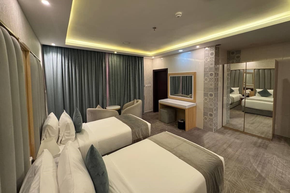 A hotel room with two beds, a desk, a chair, a mirror, and a bathroom.