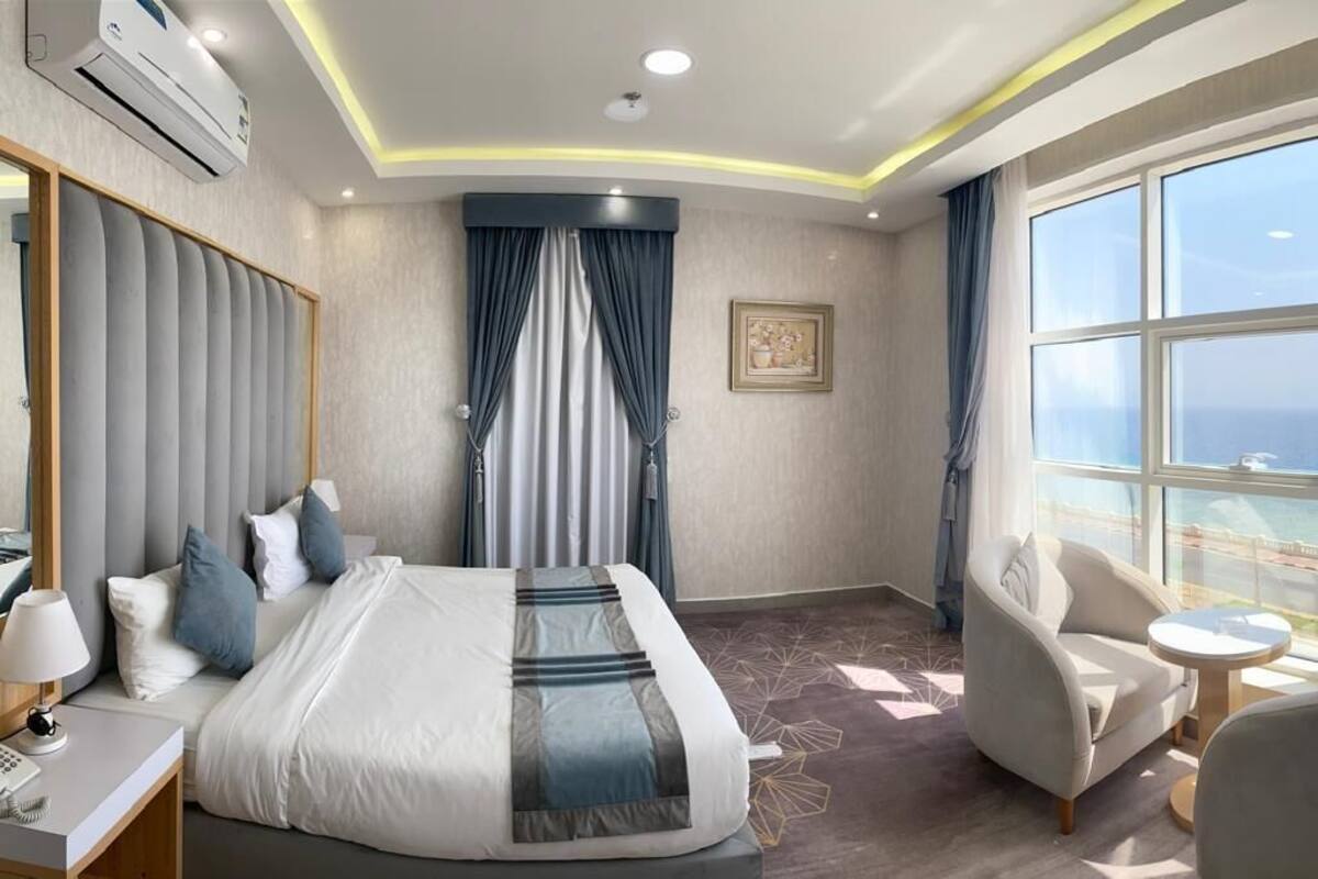 A hotel room with a large bed, a desk, a chair, and a view of the ocean.