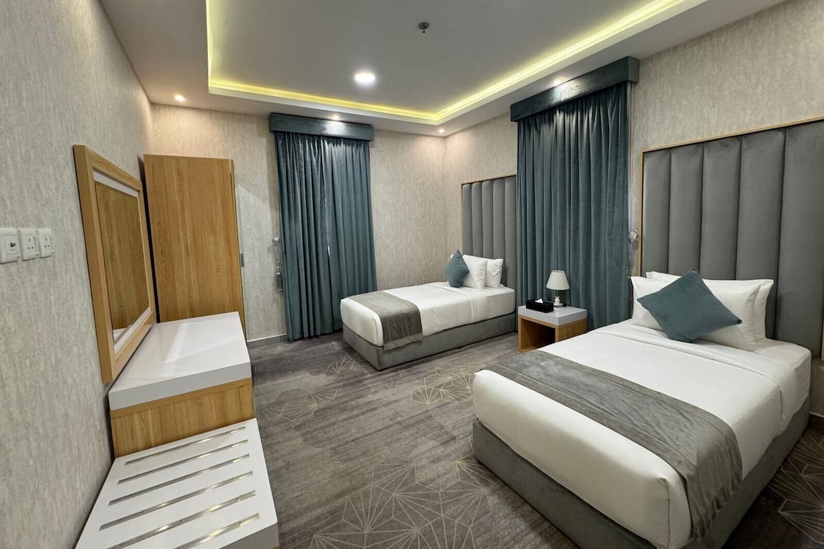 A hotel room with two beds, a wooden wardrobe, a desk, and a chair.