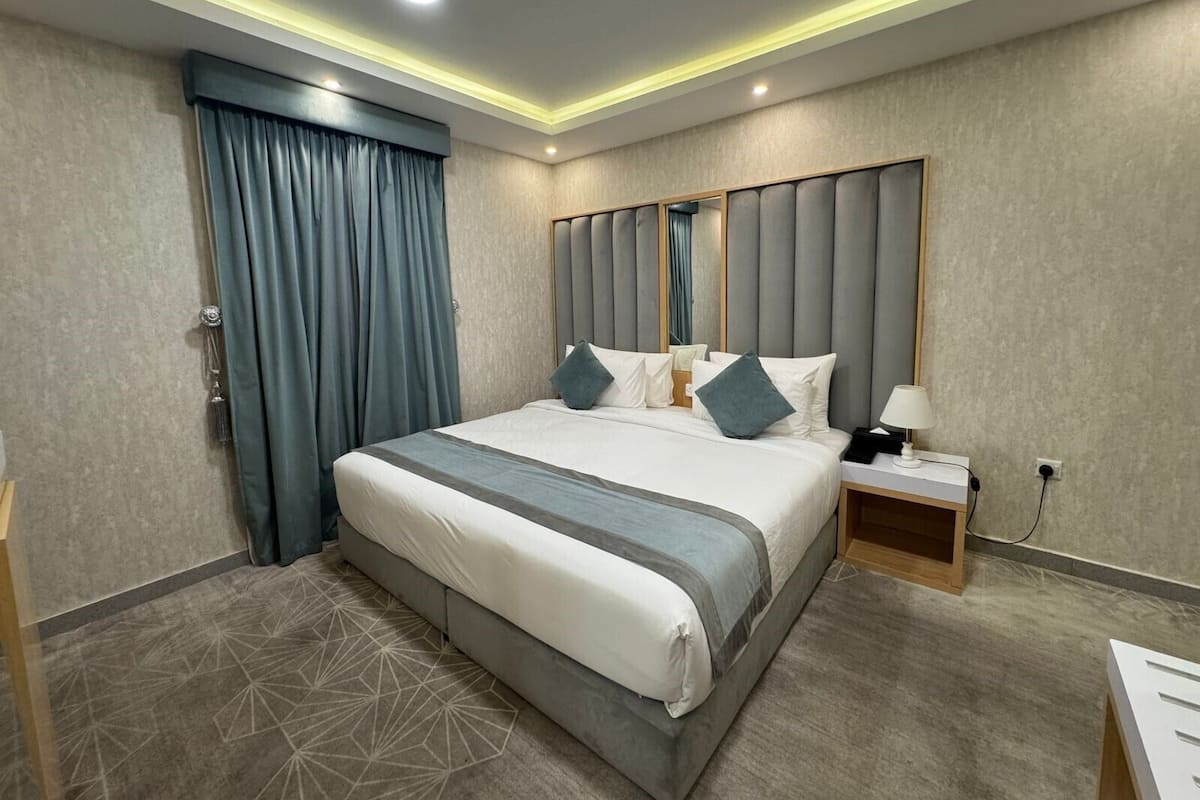 A modern hotel room with a large bed, a nightstand, a lamp, and a geometric patterned carpet.