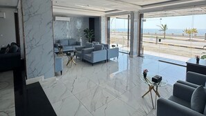A spacious living area with a large window offering a view of the sea, a marble column, and a modern sofa set. - Rose Land Hotel (Umluj)