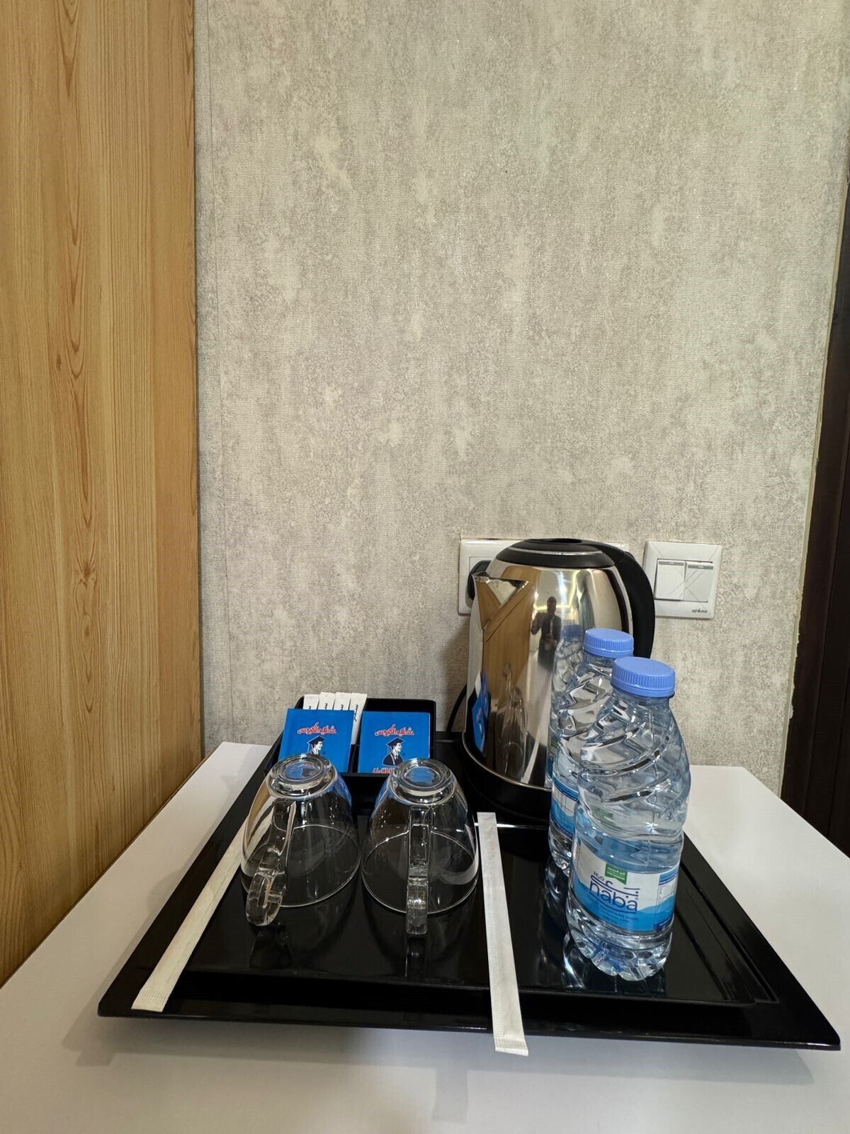 A tray with a water bottle, glasses, and a kettle on a table.