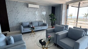 A modern living room with a grey sofa set, a glass coffee table, and a marble-patterned wall. - Rose Land Hotel (Umluj)