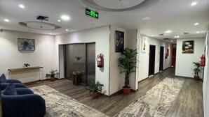 A modern hotel lobby with a central reception desk, a blue sofa, potted plants, and a patterned rug. - Rose Land Hotel (Umluj)