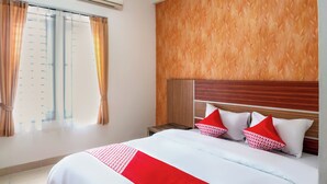 Una habitación de hotel con cama, mesita de noche y ventana con cortinas.