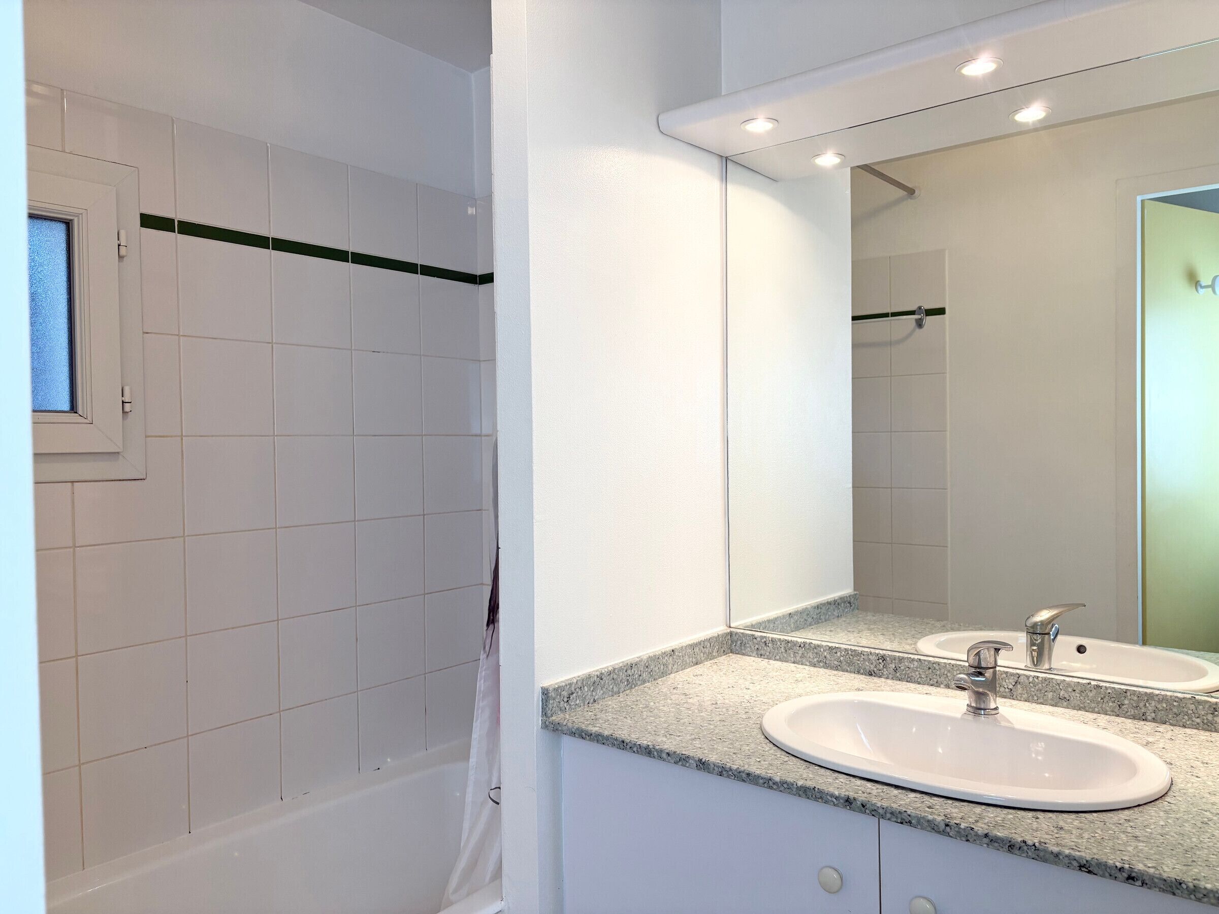 Une salle de bain moderne avec des carreaux blancs, une baignoire, un lavabo avec un miroir et un rideau de douche.
