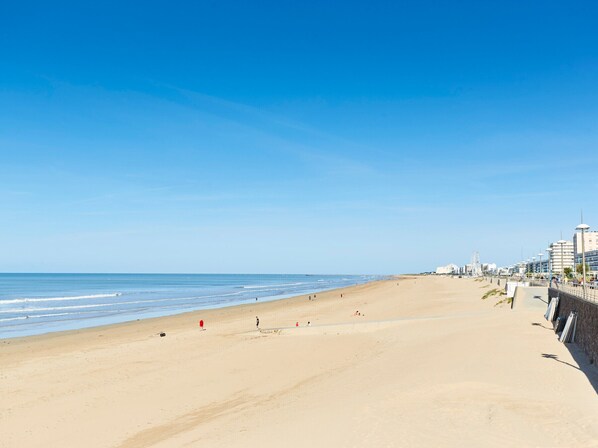 Ein weiter Sandstrand mit blauem Himmel, einigen Personen und Gebäuden im Hintergrund.