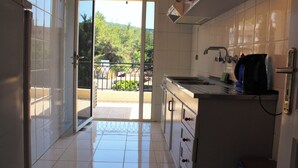 A kitchen with white cabinets, a stainless steel sink, and a view through the open door to a balcony with a railing. - Alpine hotel  (Qabr Chamoun)