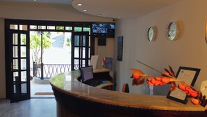 A reception desk with a computer, a clock, and a television mounted on the wall. - Alpine hotel  (Qabr Chamoun)