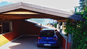 Une voiture bleue est garée sous un abri, d’où l’on peut admirer un paysage montagneux.
