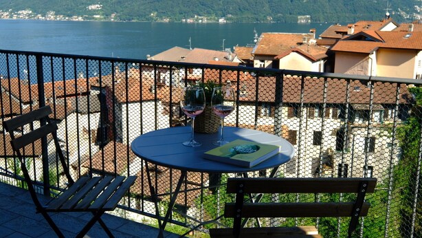 Un balcon avec une table, des chaises et un verre à vin, donnant sur un lac et des bâtiments.