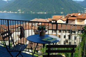Un balcon avec une table, des chaises et un verre à vin, donnant sur un lac et des bâtiments.