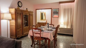 Une salle à manger avec une table dressée pour quatre personnes, un buffet en bois, une horloge, un miroir et un tableau encadré accroché au mur.