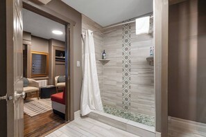 A modern bathroom with a shower, a toilet, and a sink. There is a towel rack and a bottle of shampoo on the wall.