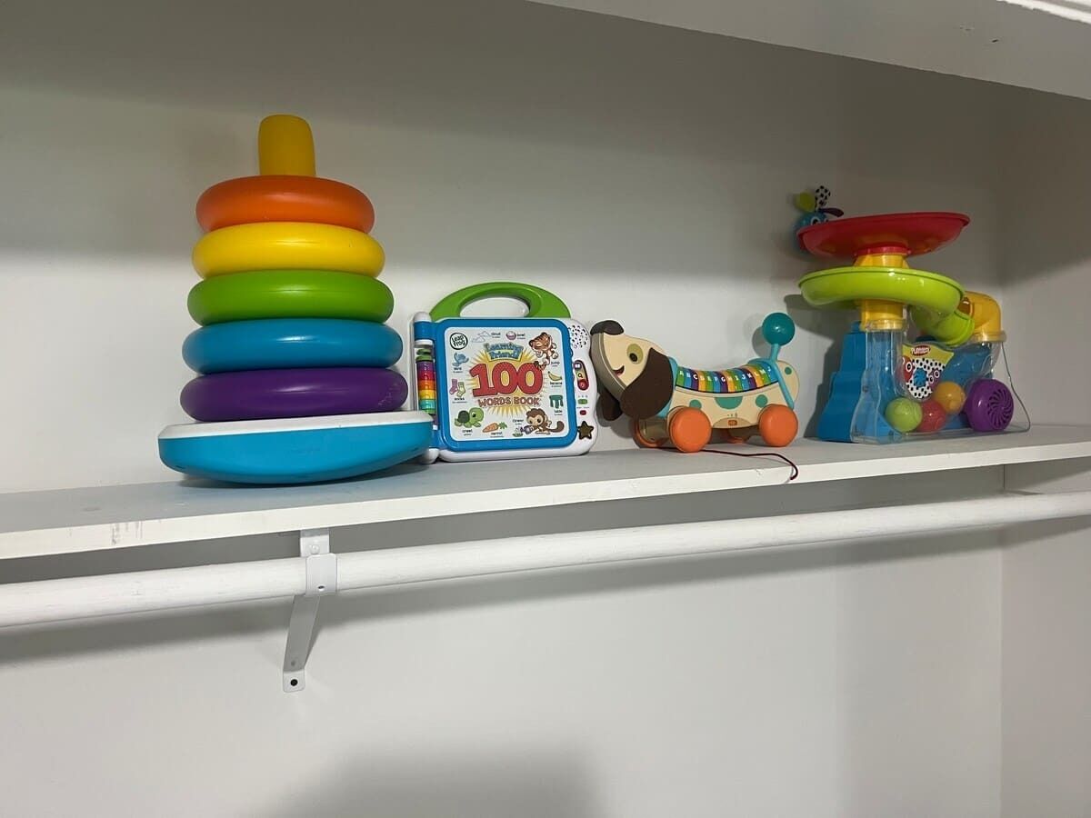 A shelf with a stack of colorful rings, a toy with a green handle, and a blue box labeled '100 WORDS BOOK'.
