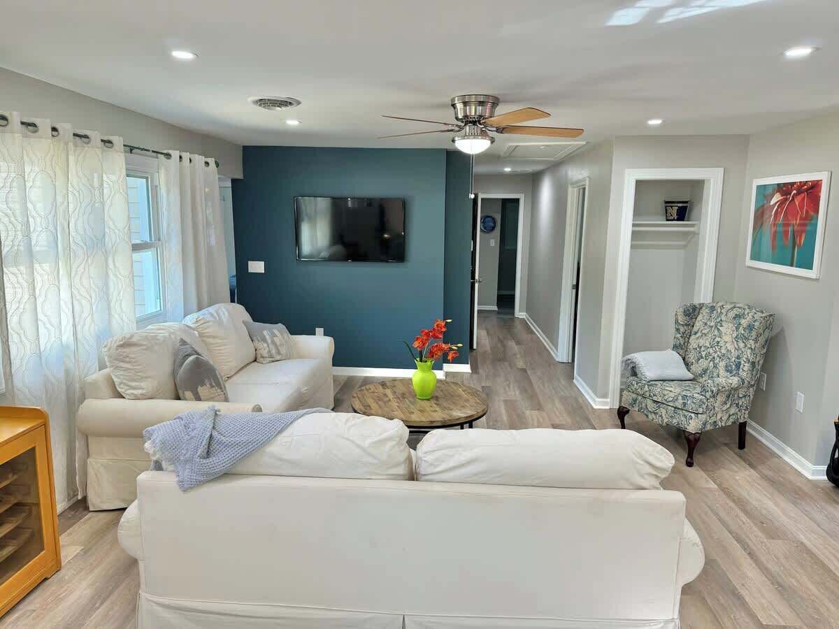 A living room with a white sofa, a patterned armchair, a wooden coffee table, and a ceiling fan.