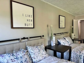 Habitación de hotel con una cama, una mesita de noche, una silla y dos carteles enmarcados en la pared.