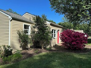 A single-story house with a red door, a small tree, and a bush in the front yard. - Family Home on Mayo Peninsula | Deck | Sleeps 10 (Edgewater)