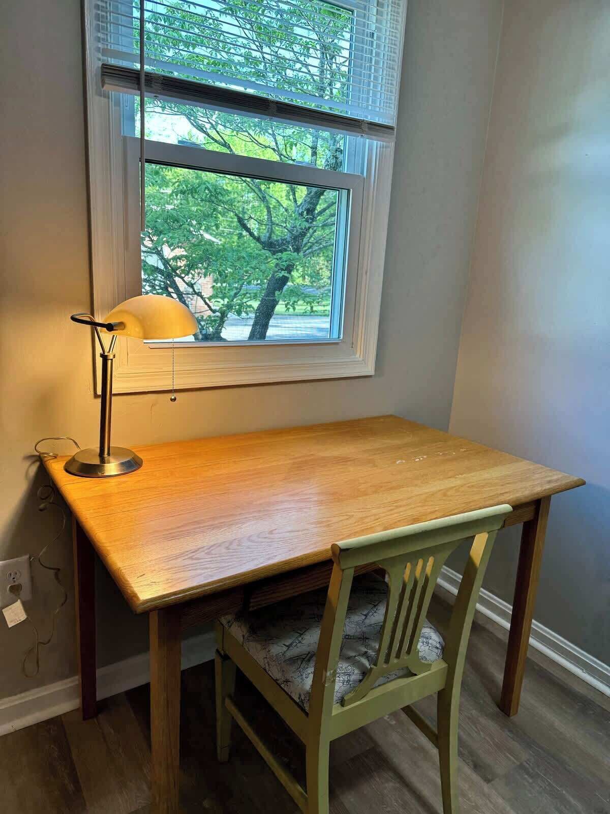 A wooden desk with a lamp, a chair, and a window with blinds.