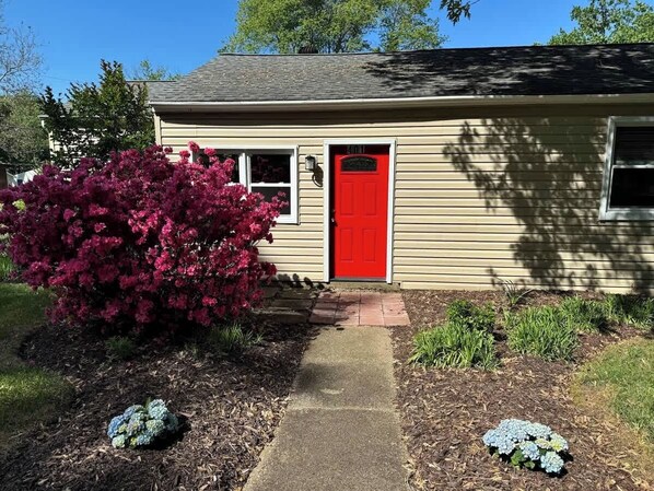 A house with a red door, a small front yard with a pathway, and a bush with pink flowers. - Family Home on Mayo Peninsula | Deck | Sleeps 10 (Edgewater)